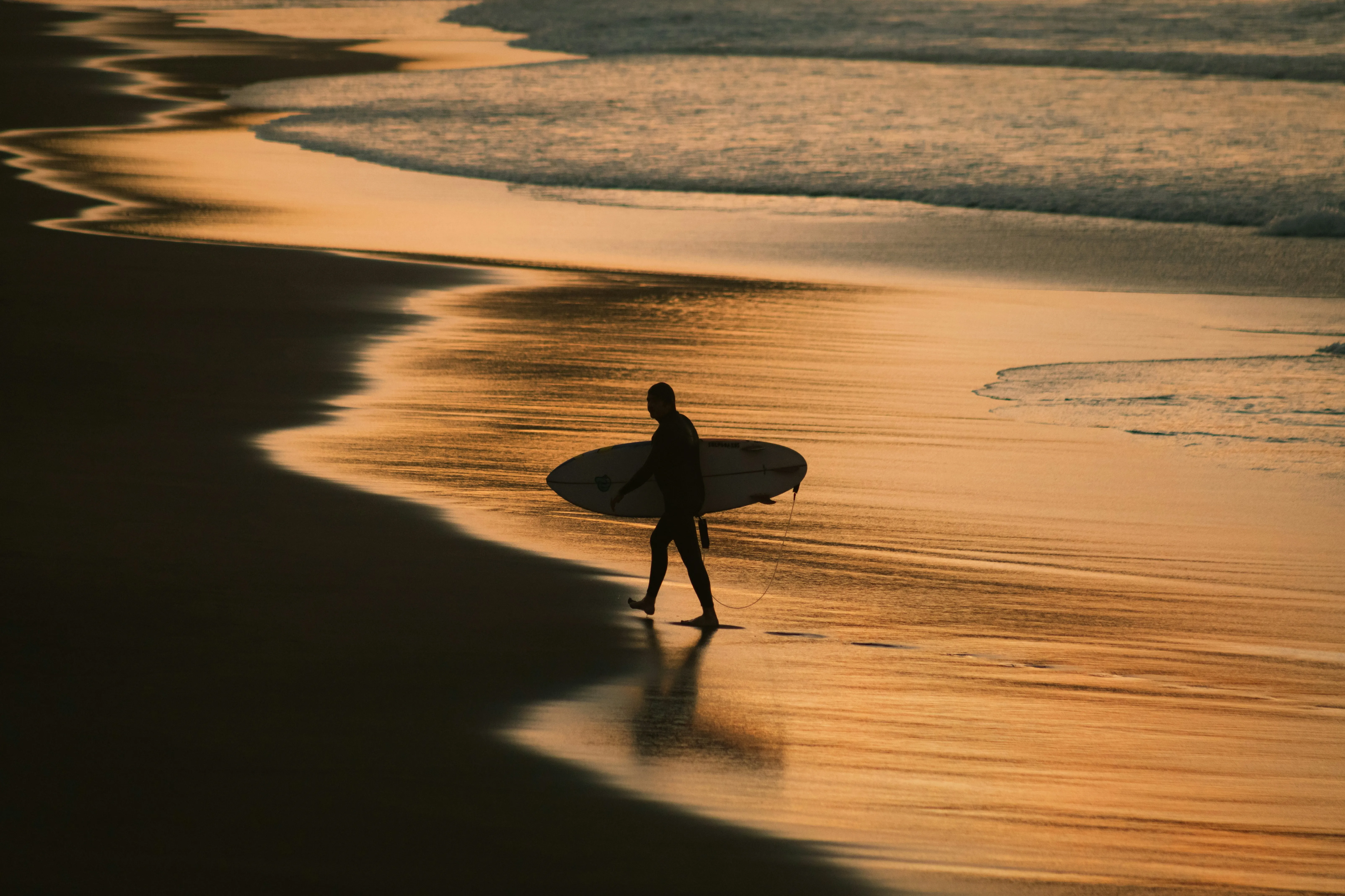 Lone surfer walking on golden sand at sunset at Playa Guiones, Nosara, Costa Rica